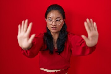 Canvas Print - Asian young woman standing over red background doing stop gesture with hands palms, angry and frustration expression