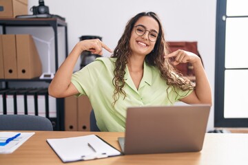 Sticker - Young hispanic woman working at the office wearing glasses looking confident with smile on face, pointing oneself with fingers proud and happy.