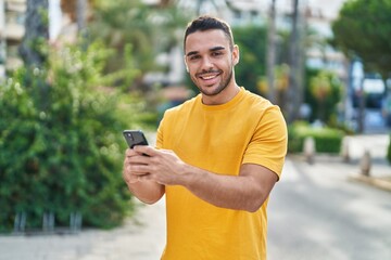 Canvas Print - Young hispanic man smiling confident using smartphone at street