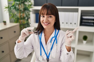 Sticker - Young brunette doctor woman holding syringe smiling happy pointing with hand and finger to the side