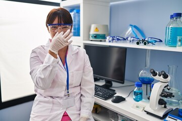 Sticker - Young brunette woman working at scientist laboratory smelling something stinky and disgusting, intolerable smell, holding breath with fingers on nose. bad smell