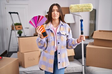 Poster - Young brunette woman painting new home walls with paint roller depressed and worry for distress, crying angry and afraid. sad expression.