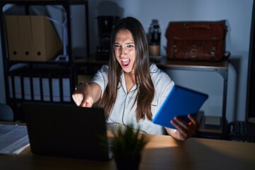 Canvas Print - Young brunette woman working at the office at night pointing displeased and frustrated to the camera, angry and furious with you