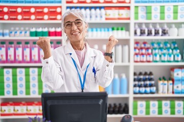 Canvas Print - Middle age woman with tattoos working at pharmacy drugstore celebrating surprised and amazed for success with arms raised and eyes closed. winner concept.