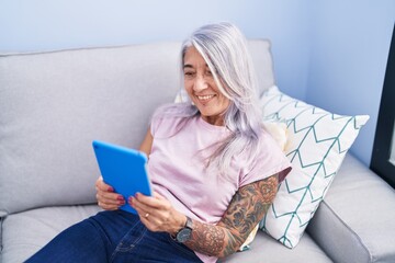 Wall Mural - Middle age grey-haired woman using touchpad sitting on sofa at home