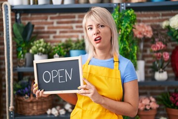 Poster - Young caucasian woman working at florist holding open sign clueless and confused expression. doubt concept.