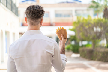 Young handsome man holding fried chips at outdoors in back position