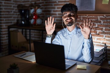 Canvas Print - Young hispanic man with beard working at the office at night showing and pointing up with fingers number ten while smiling confident and happy.