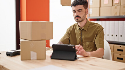 Wall Mural - Young hispanic man ecommerce business worker holding packages using touchpad at office