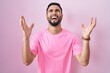 Hispanic young man standing over pink background crazy and mad shouting and yelling with aggressive expression and arms raised. frustration concept.