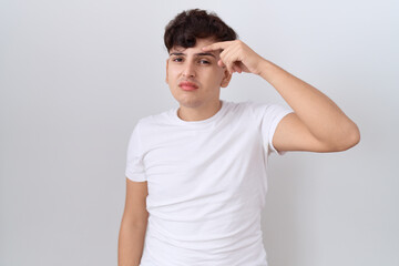 Sticker - Young non binary man wearing casual white t shirt pointing unhappy to pimple on forehead, ugly infection of blackhead. acne and skin problem