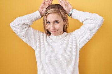 Wall Mural - Young caucasian woman wearing white sweater over yellow background doing bunny ears gesture with hands palms looking cynical and skeptical. easter rabbit concept.