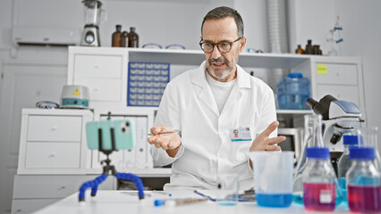 Wall Mural - Grey-haired middle-aged man scientist talking about medical research during video call in laboratory