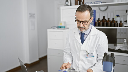 Canvas Print - Serious, grey-haired middle age man â€” a dedicated scientist engrossed in reading medical documents in his lab, surrounded by science-tech, chemistry tubes, immersed in complex analysis