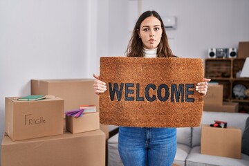 Sticker - Young hispanic woman holding welcome doormat at new home making fish face with mouth and squinting eyes, crazy and comical.