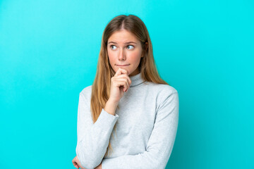 Wall Mural - Young blonde woman isolated on blue background having doubts and thinking