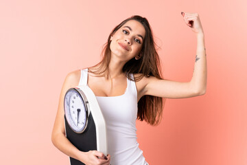 Young woman over isolated pink background holding a weighing machine and doing strong gesture