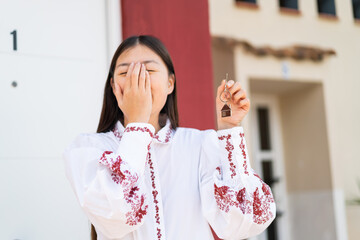 Young Chinese woman at outdoors holding home keys with happy expression