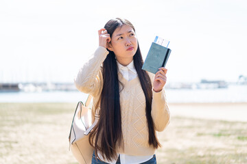 Wall Mural - Young Chinese woman holding a passport at outdoors having doubts and with confuse face expression