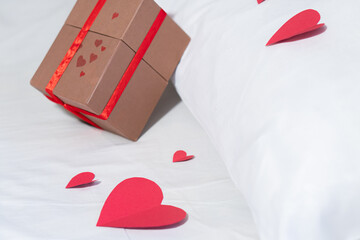 Valentine gift on bed with white bedding and red love.