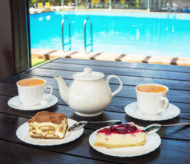 Afternoon tea set with hot tea and tasty cakes on the table and the swimming pool. Hotel resort or resting concept