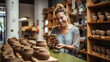 Smiling woman is browsing her smartphone in a ceramics shop, surrounded by shelves filled with various pottery items like bowls and vases.