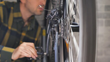 A man pedalling a mountain bike in the workshop. Close-up of a bicycle wheel and transmission. Inspection of a bike by a master, preparing a mtb for the season.