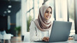 A happy muslim businesswoman in hijab at office workplace. Smiling Arabic woman working on laptop in a modern office.