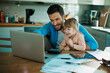 © Geber86 - Smiling young man looking at laptop with little daughter with paperwork on desk