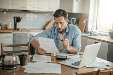 Serious young man reading bill document at home