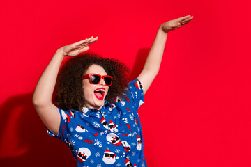 Photo portrait of pretty young girl raise hands dancing have fun dressed stylish blue x-mas print outfit isolated on red color background