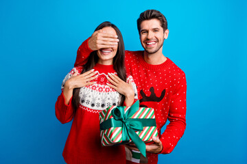 Poster - Photo portrait of lovely young spouses hold gift cover eyes surprise wear x-mas ornament red sweaters isolated on blue color background