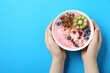 Woman holding tasty smoothie bowl with fresh kiwi fruit, berries and granola at light blue table, top view. Space for text