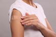 © New Africa - Woman with sticking plaster on arm after vaccination against light grey background, closeup