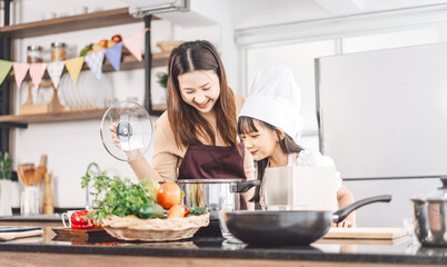 Mother and daughter cooking in kitchen preparation food for dinner meal, lifestyles together child with parent