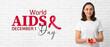Leinwandbild Motiv Young woman with red ribbon on white brick background. World AIDS Day