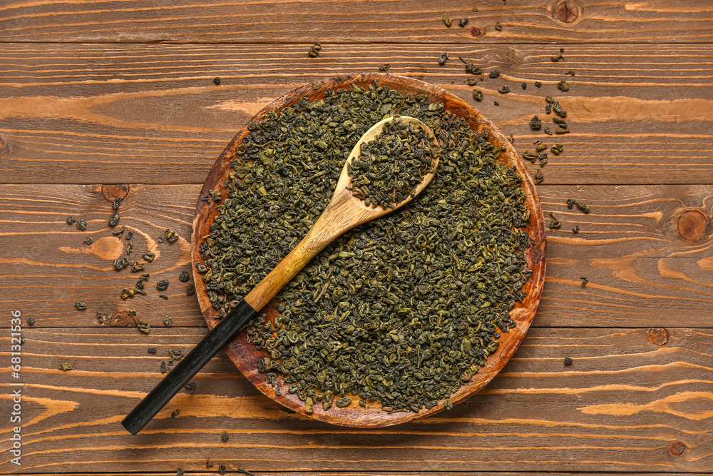 Spoon and tray with green tea leaves on wooden background