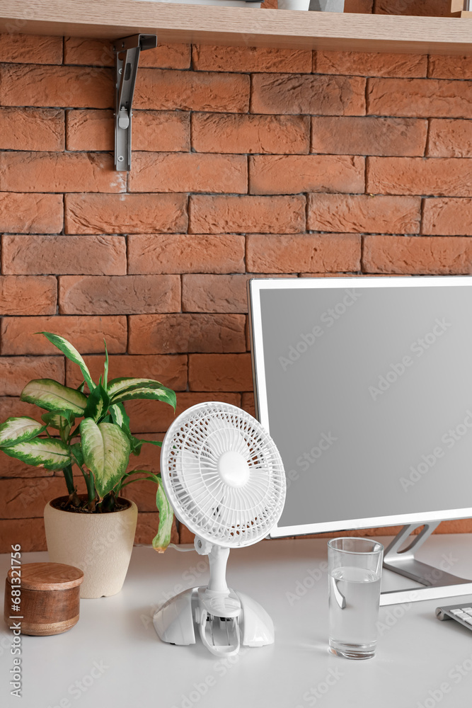 Electric fan and glass of water on table with modern computer