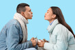 Happy couple in warm clothes with mugs of tasty mulled wine kissing on blue background