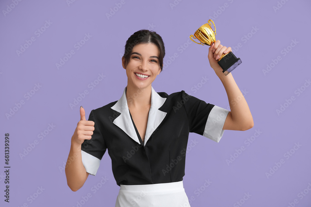 Young chambermaid with gold cup showing thumb-up on lilac background