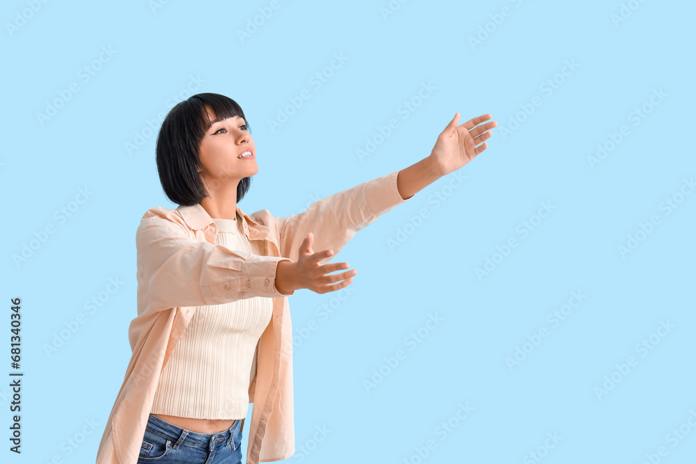 Young woman opening arms for hug on blue background