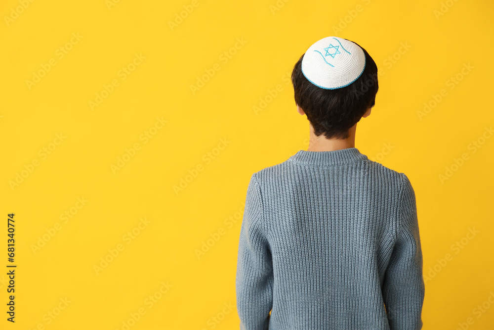 Little Israeli boy in kipa on yellow background, back view