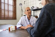 © Natee Meepian - Senior woman doctor wear white medical uniform holding hand of female patient having disease health problem give support help empathy and people healthcare concept
