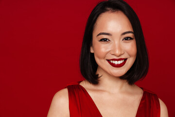 Wall Mural - Beautiful asian woman smiling at camera while standing isolated over red background