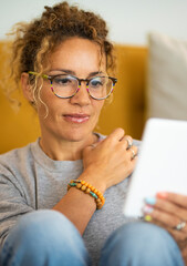 Happy relaxed adult cute woman use electronic device reader to read an e-book and enjoy her indoor leisure activity at home. Pretty female people wearing glasses and smile. Portrait of lady