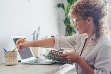 Wall Mural - Modern young pretty adult lady working at home in alternative office work place with laptop computer and notebook taking notes. Indoor apartment leisure job activity female people using technology