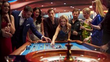 Gathering Of Wealthy Young Individuals, Standing Together Around A Roulette Table In A Contemporary Casino Setting. Cinematic Nightlife Footage, Carefree Gamblers Congratulating The Winning Players