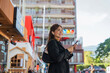 © Natee Meepian - Asian professional businesswoman holding cellphone using smartphone standing or walking on big city urban street outside. Successful Asian business woman