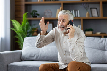 upset and angry senior man talking on the phone at home, sitting on the sofa and expressively explai