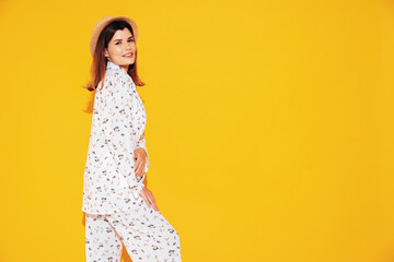 Wall Mural - Young beautiful smiling female in trendy summer costume clothes. Carefree woman posing near yellow wall in studio. Positive model having fun indoors. Cheerful and happy. In hat